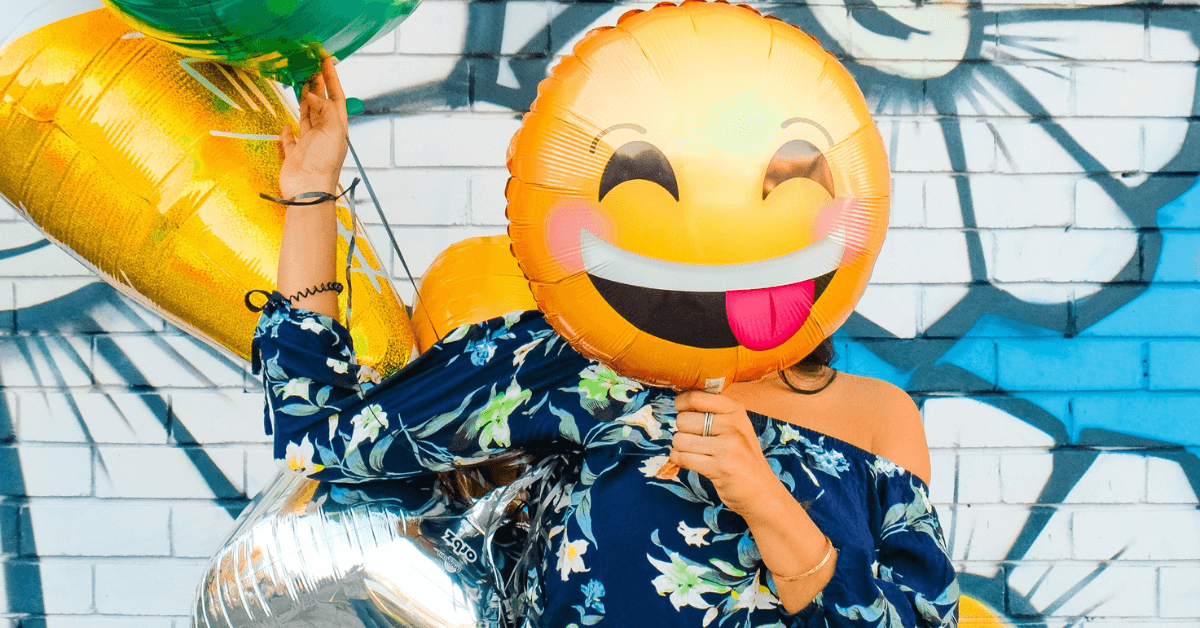 Woman with a laughing emoji balloon in front of her face.