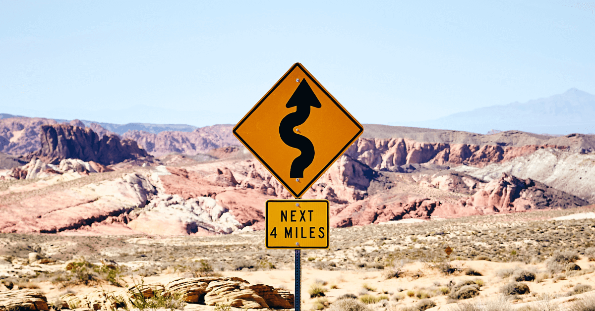 Road sign in a desert that warns of twisty road for the next 4 miles