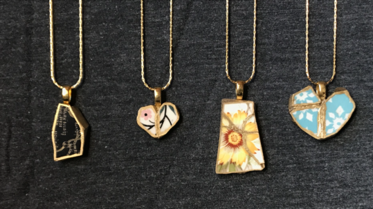 Four necklaces hanging in a row, all made of varying colors and textures, with cracks that have been fit back together and edged with gold.