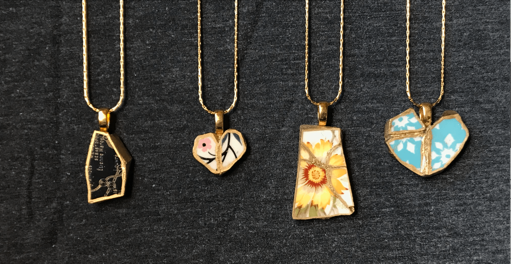 Four necklaces hanging in a row, all made of varying colors and textures, with cracks that have been fit back together and edged with gold.