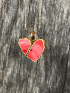 A necklace with a pick heart pendant made of broken dishes, with a crack down the middle mended with gold. 